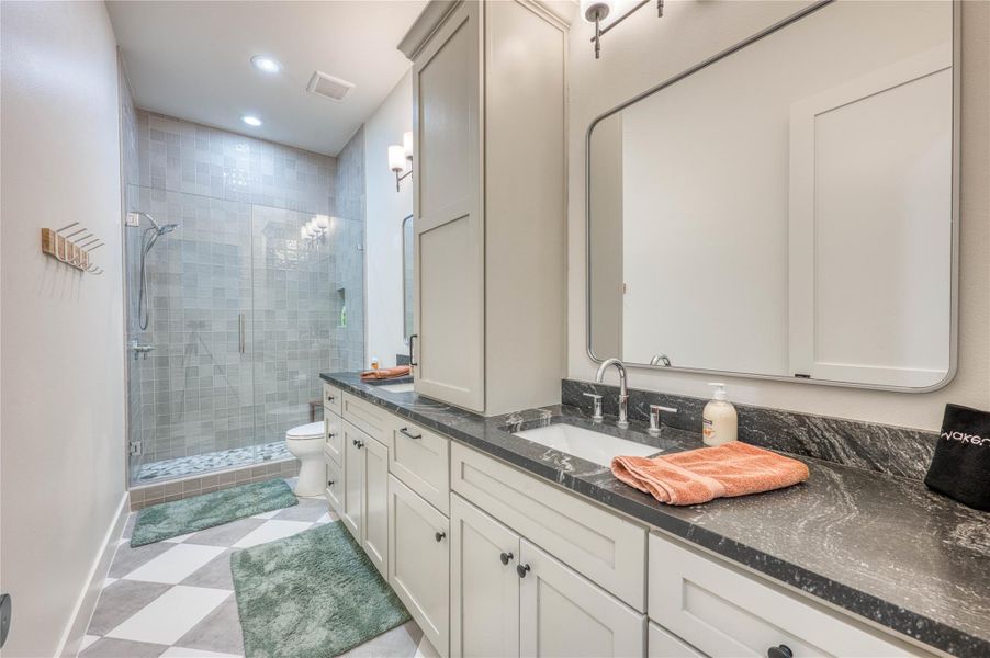 Spacious bathroom featuring a dual vanity with undermount sinks, stone countertops, a large framed mirror, and a glass-enclosed shower with tiled walls and a pebble-style floor