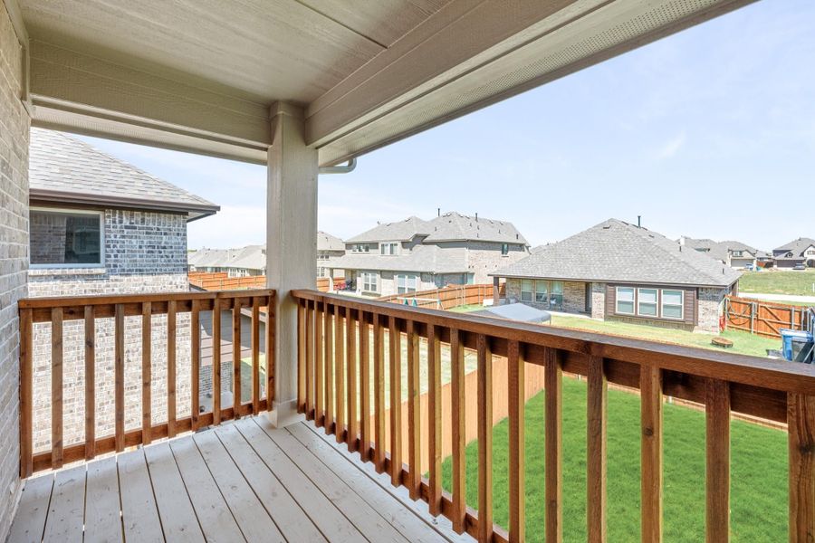 Covered balcony with wood railing overlooking a fenced backyard and neighboring homes in a subdivision Covered balcony with wood railing overlooking a fenced backyard and neighboring homes in a subdivision