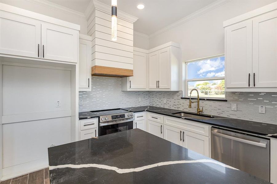 Kitchen with tasteful backsplash, crown molding, white cabinets, stainless steel appliances, and a sink