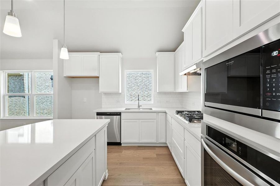 Kitchen with stainless steel appliances, white cabinets, pendant lighting, light wood-type flooring, and decorative backsplash