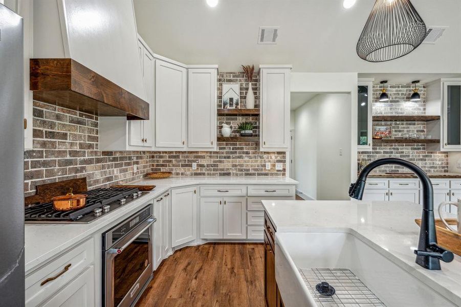 Kitchen with appliances with stainless steel finishes, wood-type flooring, white cabinets, and custom range hood