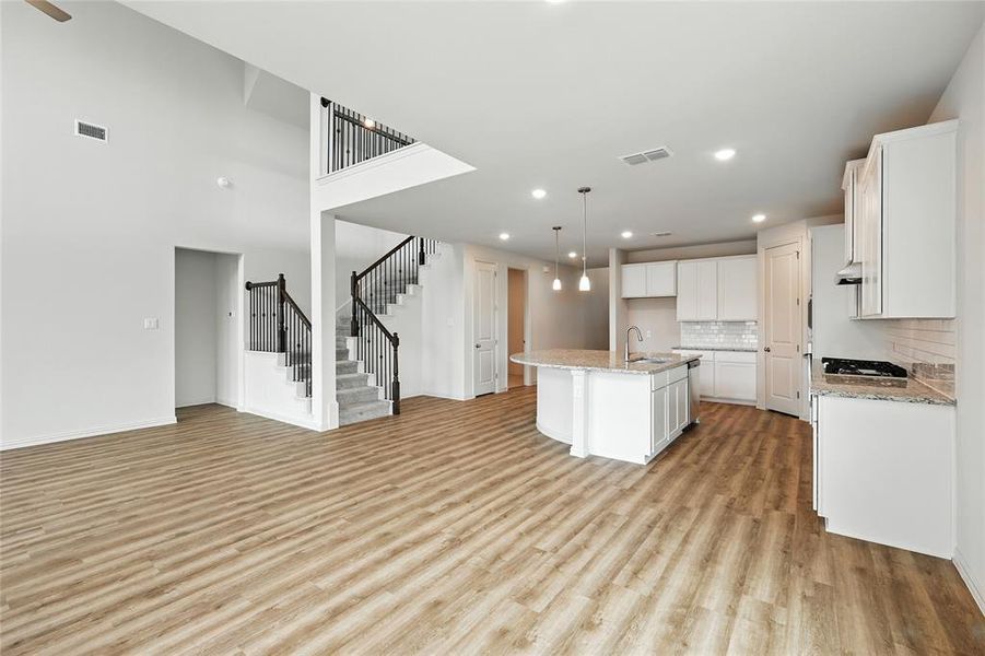 Kitchen with white cabinets, open floor plan, a center island with sink, tasteful backsplash, and light wood-style flooring