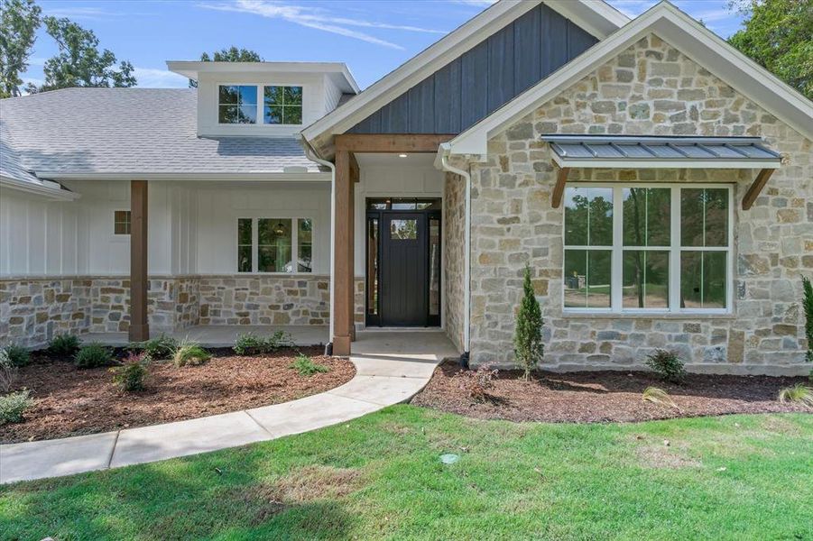 Property entrance featuring stone siding, board and batten siding, a porch, and a lawn Property entrance featuring stone siding, board and batten siding, a porch, and a lawn