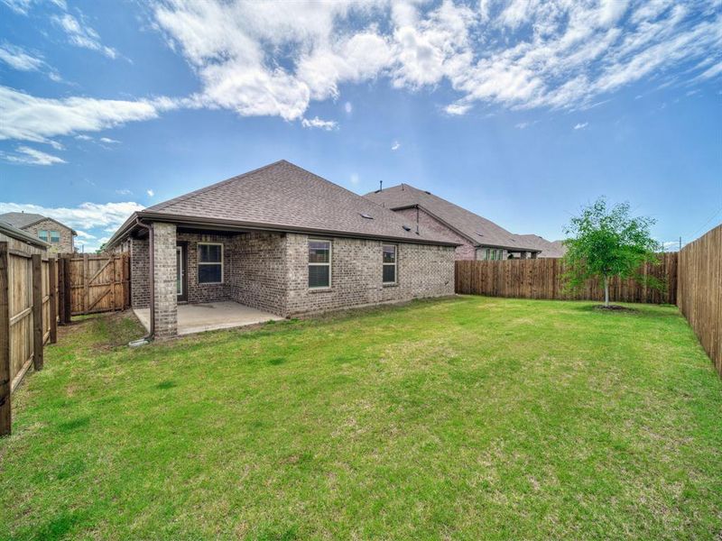 Back of house with a shingled roof, a patio area, a yard, a fenced backyard, and brick siding