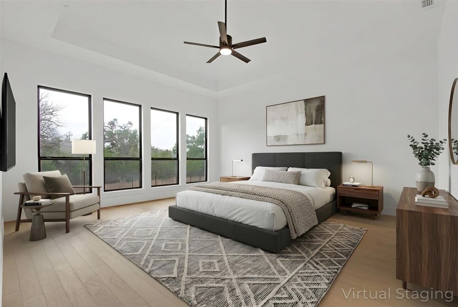 Virtually-Staged Primary Bedroom featuring a raised ceiling, light hardwood floors,  ceiling fan, and scenic, greenbelt view