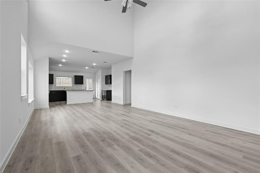 Unfurnished living room with ceiling fan, a high ceiling, recessed lighting, light wood-style floors, and a fireplace