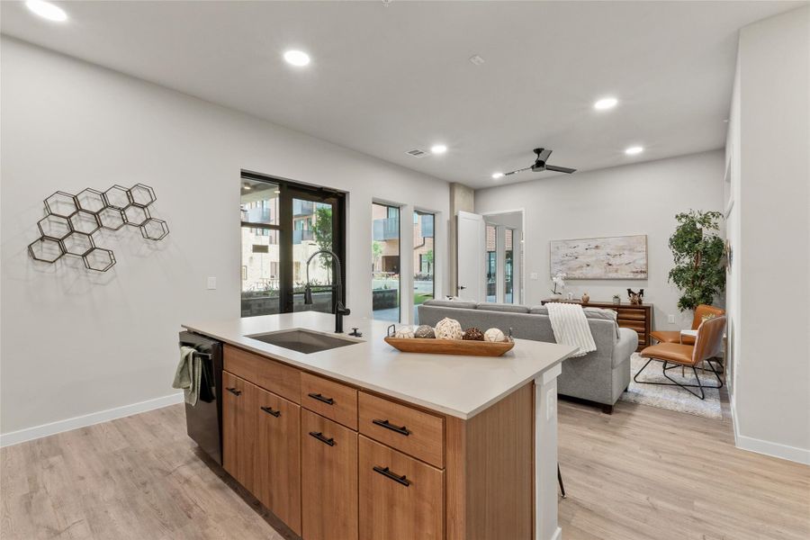 Kitchen featuring light wood-style floors, dishwashing machine, ceiling fan, light countertops, and a kitchen island with sink