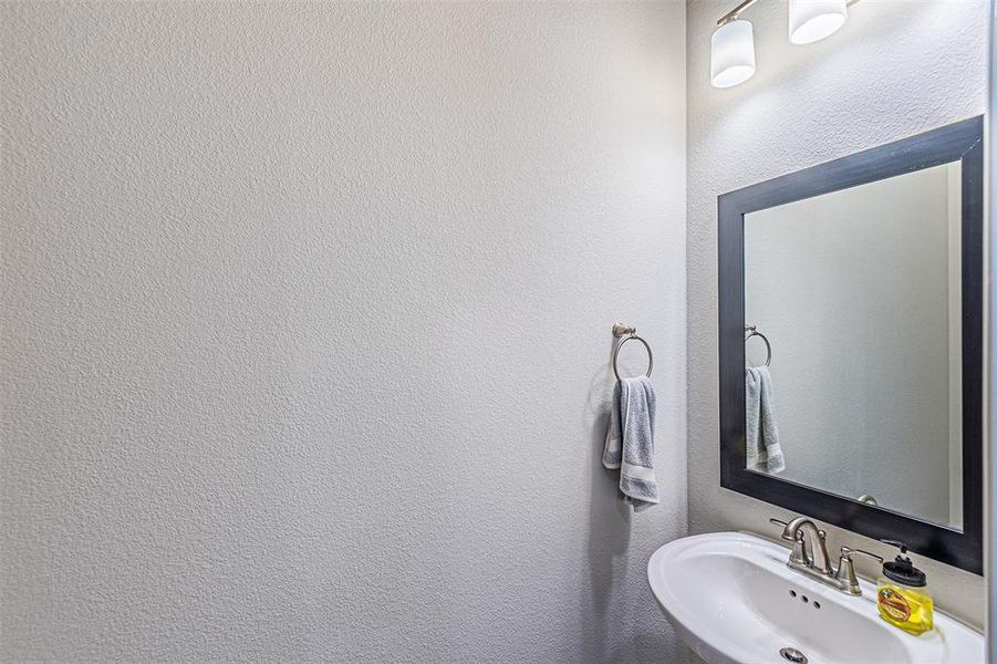 Pedestal sink with a dual-handle faucet, framed mirror, and wall-mounted lighting fixture