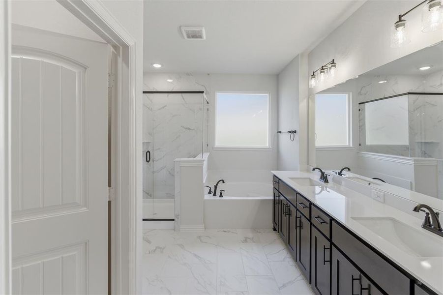 Bathroom featuring double vanity, a bath, light marble finish flooring, and a marble finish shower