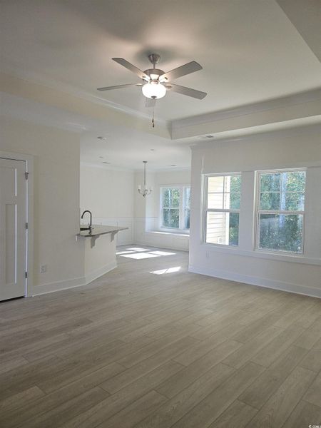 Unfurnished living room with light wood finished floors, ornamental molding, ceiling fan, a wainscoted wall, and a chandelier Unfurnished living room with light wood finished floors, ornamental molding, ceiling fan, a wainscoted wall, and a chandelier