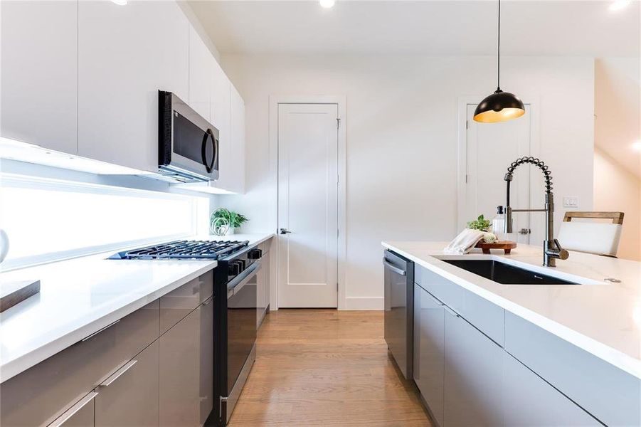 Kitchen with white cabinets, decorative light fixtures, light wood-type flooring, sink, and stainless steel appliances