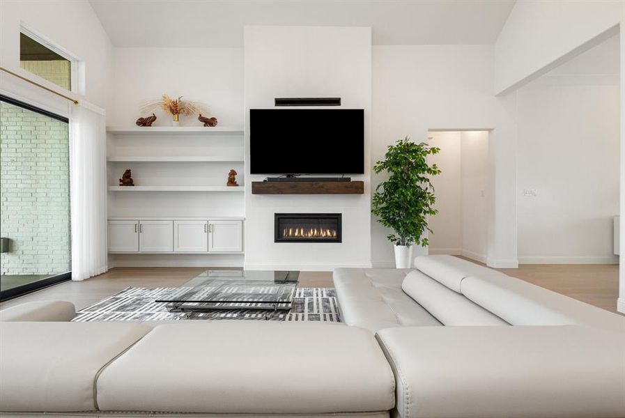 Living area featuring light wood finished floors, a glass covered fireplace, and lofted ceiling