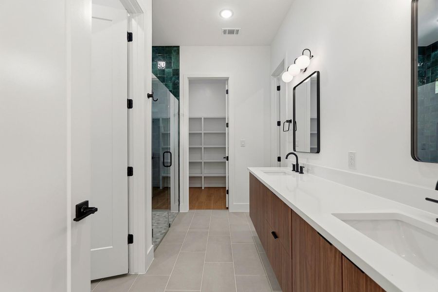 Bathroom featuring double vanity, a stall shower, a spacious closet, and light tile patterned flooring