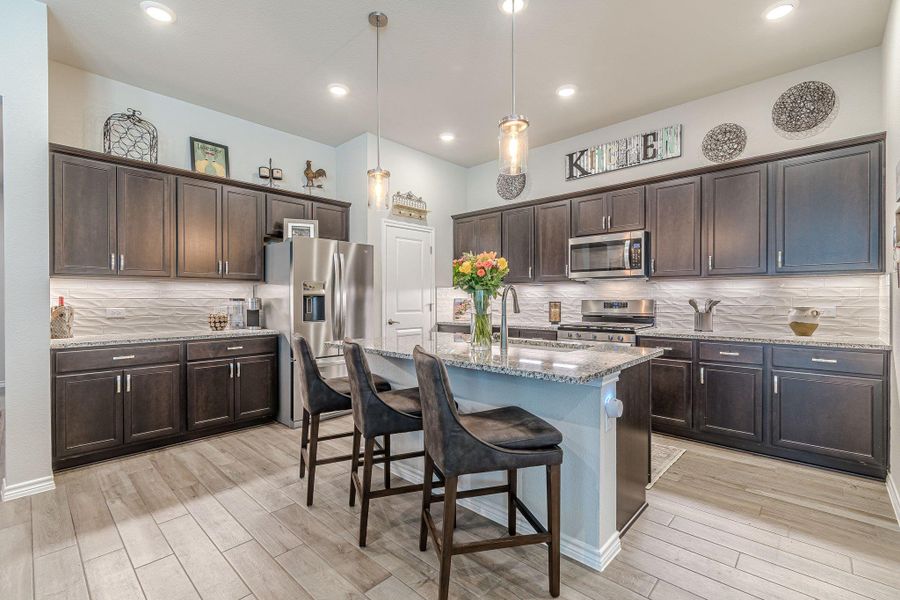 Kitchen featuring stainless steel appliances, a sink, light wood-type flooring, backsplash, and dark brown cabinetry