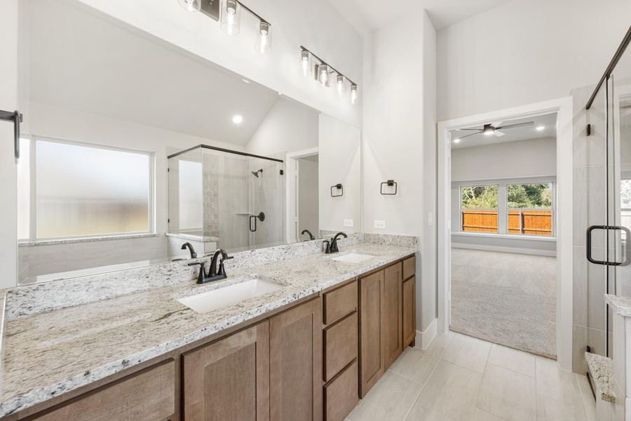 Master bathroom with double vanity, granite countertops, wood cabinets, and glass shower enclosure