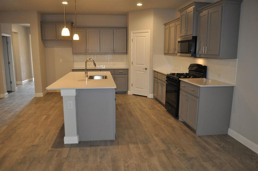 Kitchen featuring sink, a kitchen island with sink, gas stove, dark hardwood / wood-style flooring, and decorative light fixtures