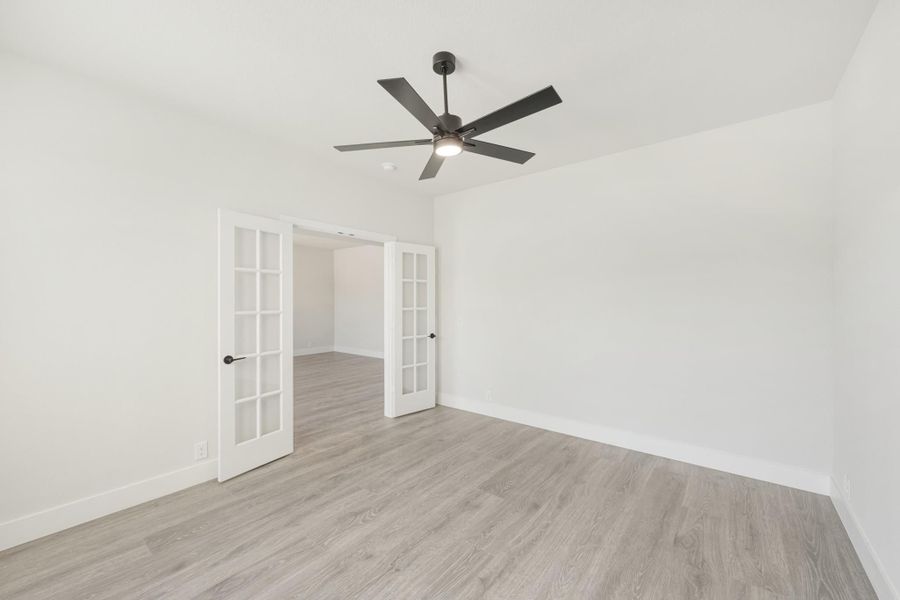 Empty room with light wood floors, ceiling fan, and white French doors