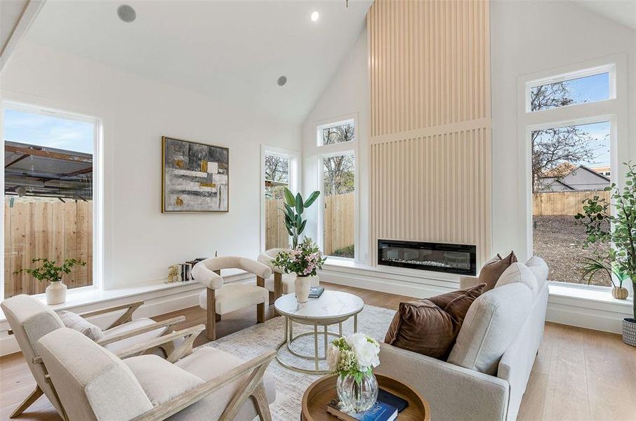 Living area featuring high vaulted ceiling, a glass covered fireplace, light wood-style floors, and healthy amount of natural light