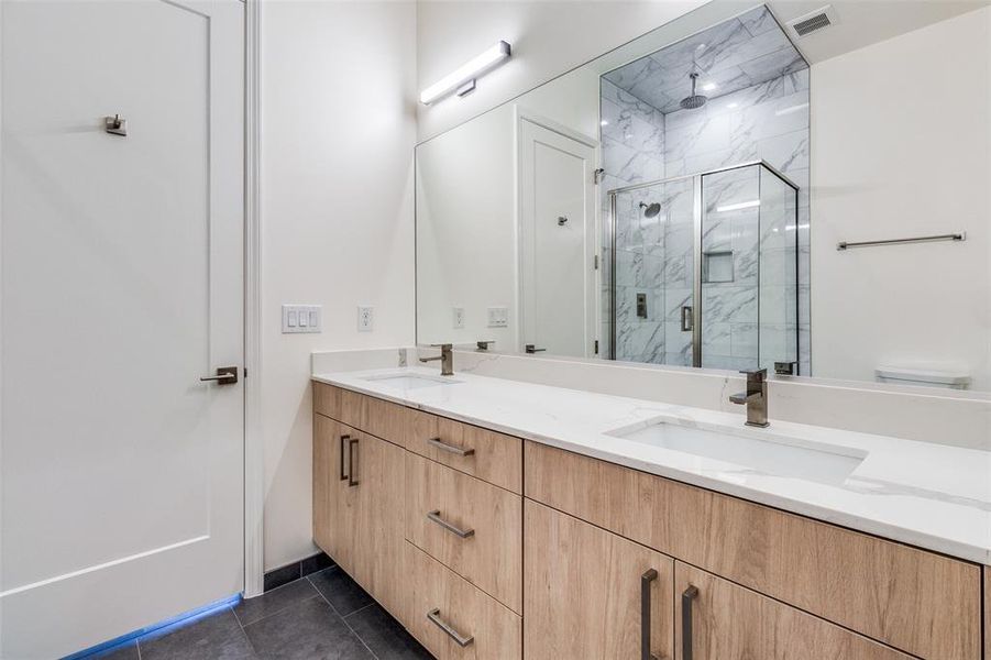 Bathroom featuring an enclosed shower, double vanity, and tile flooring