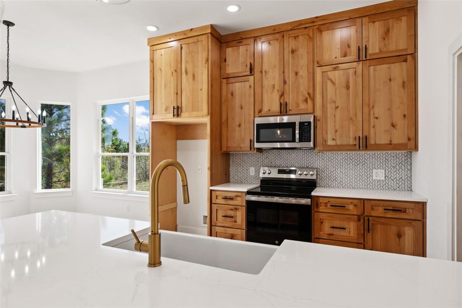 Kitchen with stainless steel appliances, light stone counters, pendant lighting, decorative backsplash, and recessed lighting