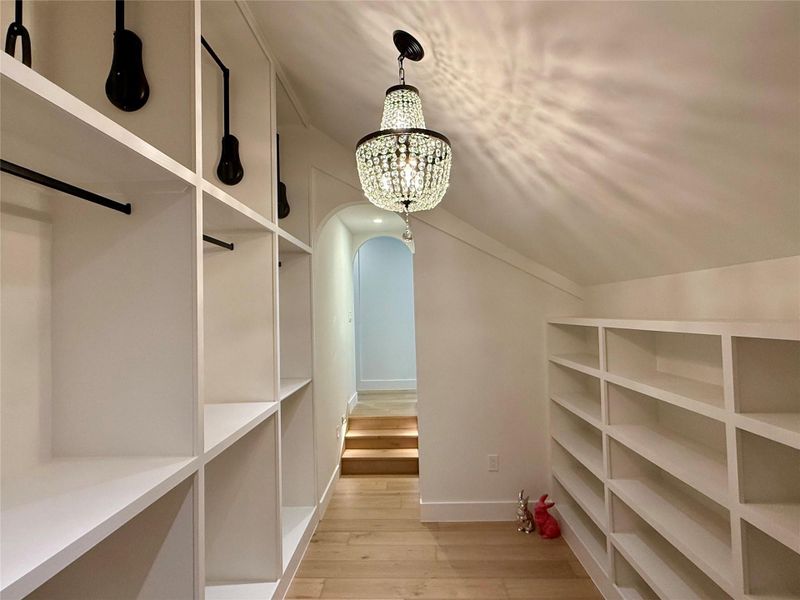 Spacious closet featuring arched walkways, light wood-style floors, a chandelier, and lofted ceiling Spacious closet featuring arched walkways, light wood-style floors, a chandelier, and lofted ceiling