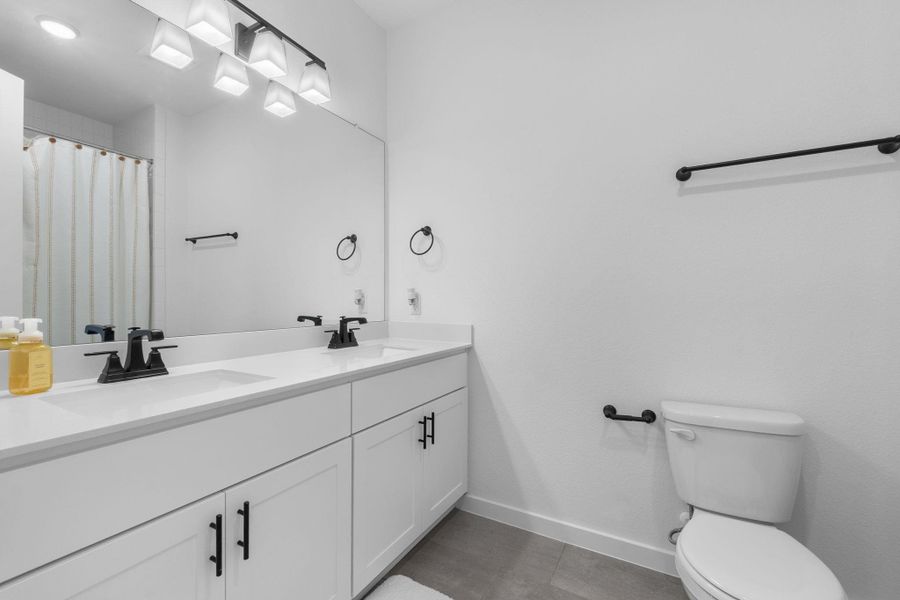 Bathroom 3 with double vanity, toilet, baseboards, and a sink