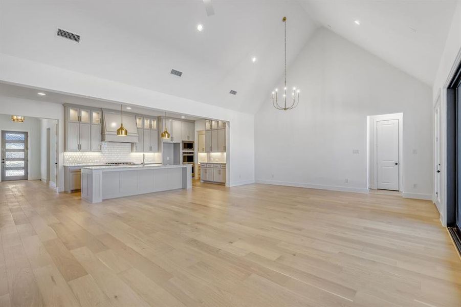 Unfurnished living room with a high ceiling, light wood-style floors, and hanging lights
