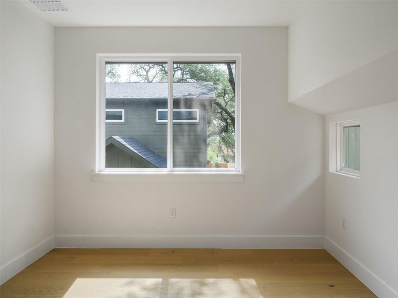 Bright interior space featuring a large picture window, a secondary window, light wood-finish flooring, white walls, and white trim