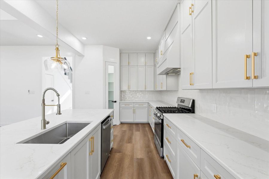 B quartz countertops and elegant gold hardware bring this kitchen to life, complemented by a stainless steel five-burner gas stove, and dishwasher.