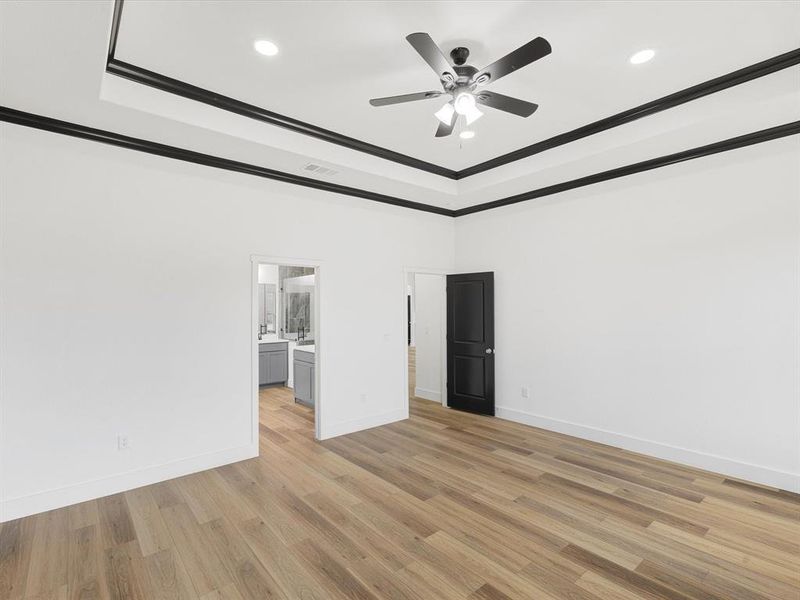 Unfurnished bedroom with light wood finished floors, ornamental molding, a ceiling fan, recessed lighting, and a raised ceiling Unfurnished bedroom with light wood finished floors, ornamental molding, a ceiling fan, recessed lighting, and a raised ceiling