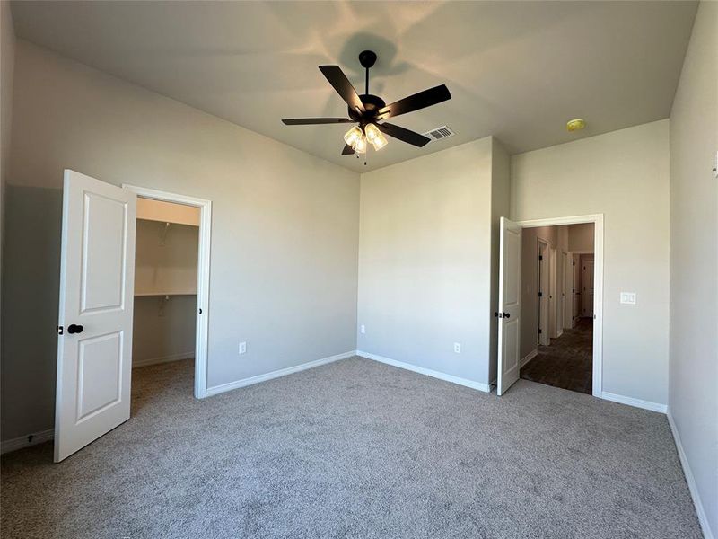 Unfurnished bedroom featuring a walk in closet, light carpet, and a ceiling fan Unfurnished bedroom featuring a walk in closet, light carpet, and a ceiling fan