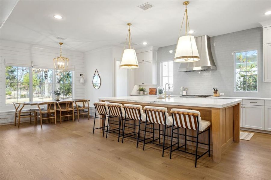 Kitchen with light wood-type flooring, wall chimney range hood, plenty of natural light, and visible vents Kitchen with light wood-type flooring, wall chimney range hood, plenty of natural light, and visible vents