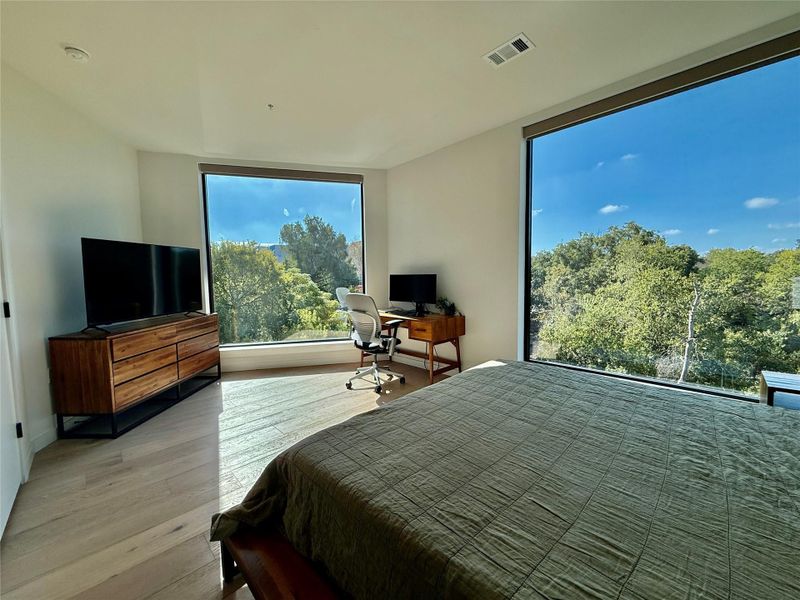 Floor-to-ceiling windows offer serene treetop vistas, bathing this bedroom in natural light.