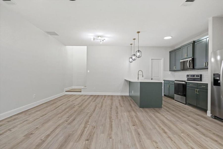 Kitchen featuring decorative backsplash, appliances with stainless steel finishes, light wood-type flooring, and pendant lighting