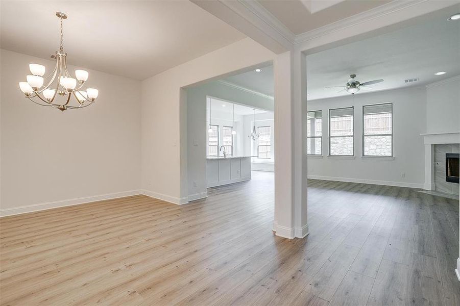 Unfurnished living room with a tiled fireplace, ceiling fan with notable chandelier, light wood-type flooring, and plenty of natural light