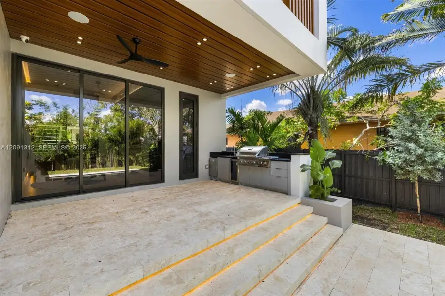 Covered patio featuring a wood-finished tongue-and-groove ceiling with recessed lighting, integrated outdoor kitchen with stainless steel grill, stone-tile flooring, and tiered staircase with step-level lighting Covered patio featuring a wood-finished tongue-and-groove ceiling with recessed lighting, integrated outdoor kitchen with stainless steel grill, stone-tile flooring, and tiered staircase with step-level lighting
