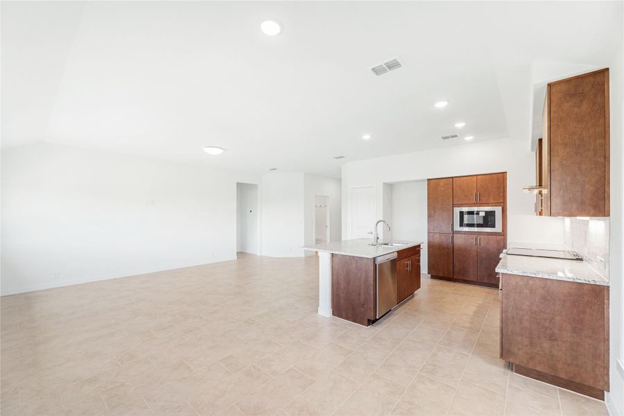 Open-concept kitchen with dark wood cabinets, center island with sink, and stainless steel appliances on tile floors