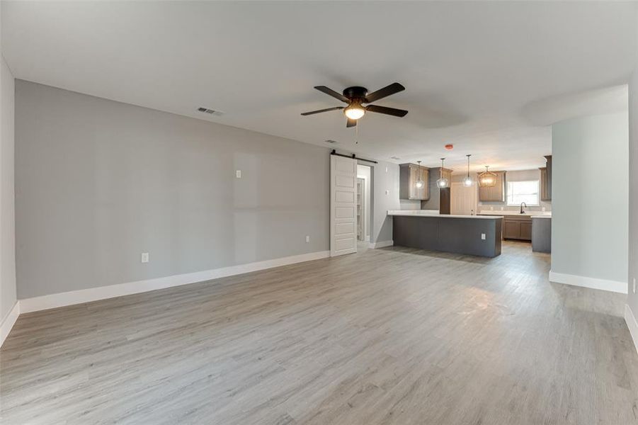 Unfurnished living room featuring a barn door, light wood-type flooring, sink, and ceiling fan