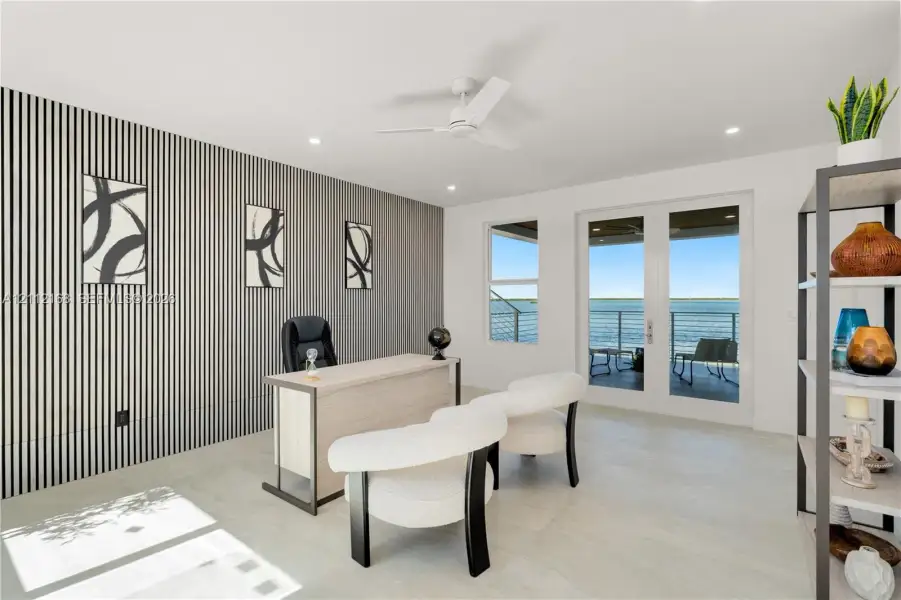 Accent wall with vertical paneling, light-toned flooring, white ceiling fan, and double glass doors providing external water-front access Accent wall with vertical paneling, light-toned flooring, white ceiling fan, and double glass doors providing external water-front access