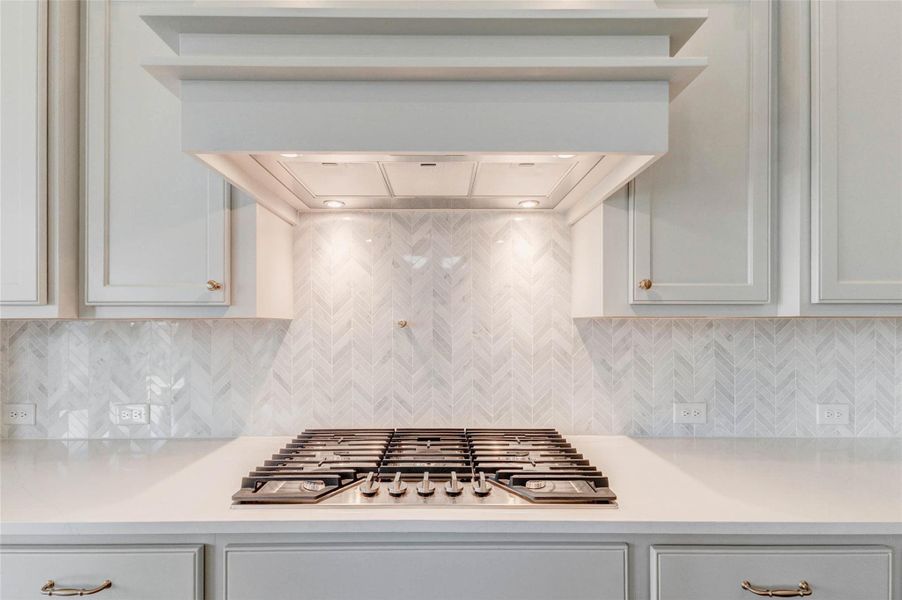 Sleek gas cooktop with a stylish herringbone tile backsplash.