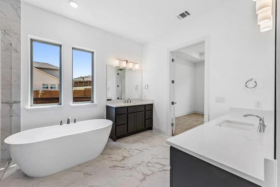 Bathroom with a soaking tub, vanity, light marble finish flooring, two sinks, and recessed lighting