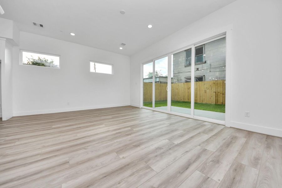 This photo showcases a bright, open living space with light wood flooring and large sliding glass doors leading to a fenced backyard. The room has high ceilings and modern recessed lighting, creating an inviting atmosphere.
