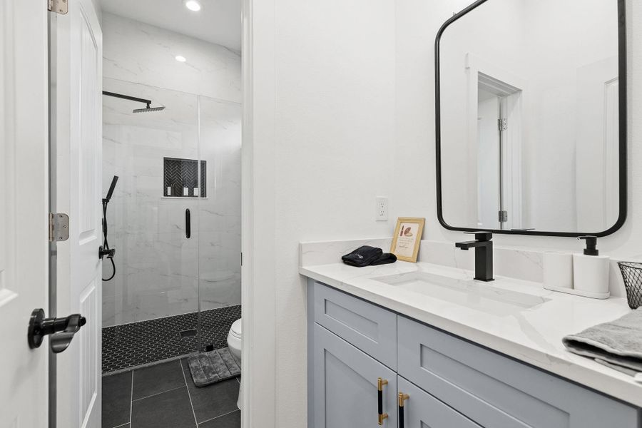 Bathroom featuring a marble finish shower, vanity, and dark tile patterned flooring