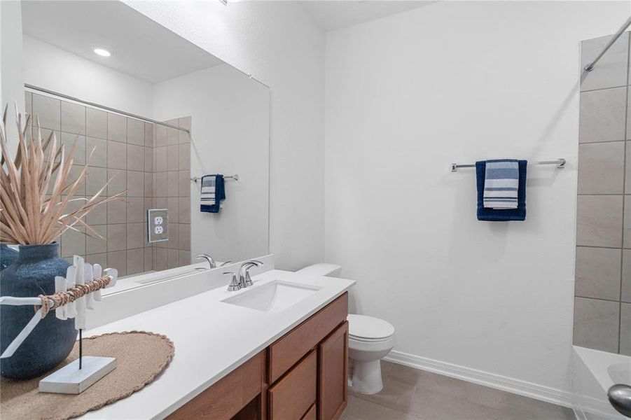 Secondary bath features tile flooring, bath/shower combo with tile surround, stained wood cabinets, beautiful light countertops, mirror, sleek fixtures and modern finishes.