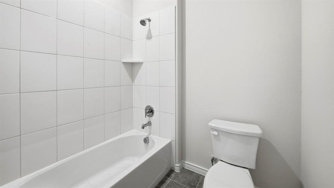 White tiled tub and shower combination with chrome fixtures and an integrated corner shelf
