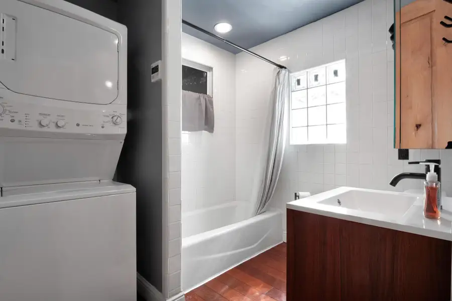 Full bath with stacked washer / drying machine, shower / bath combo, wood finished floors, and vanity