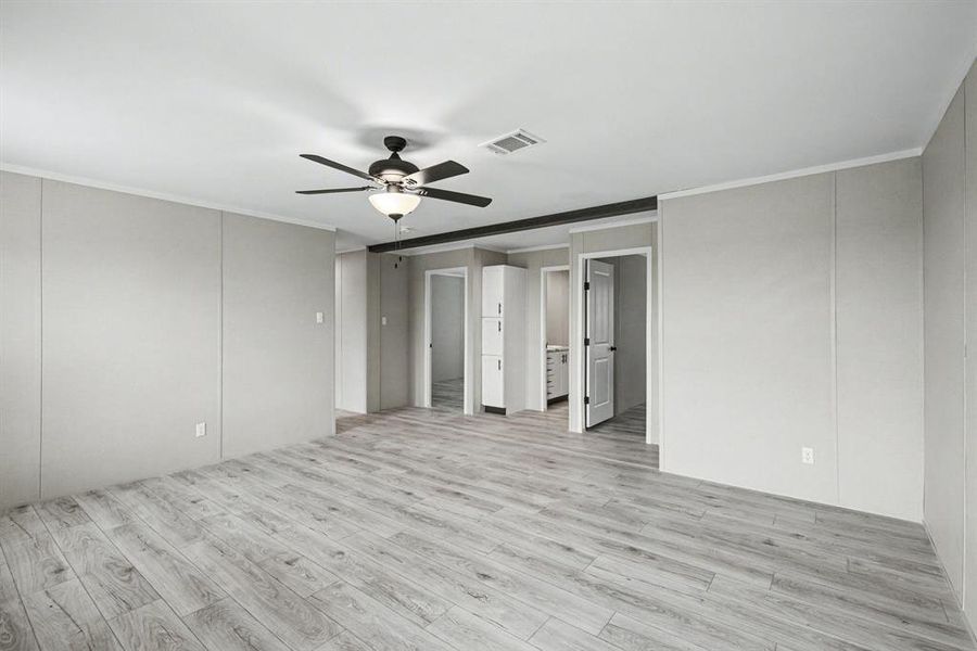 Spacious flex-room featuring wood-look flooring, light-toned wall paneling, a ceiling fan with integrated lighting, and white trim molding.  In this view, you can see the additional 3-door storage/ linen closet just outside the secondary bathroom.