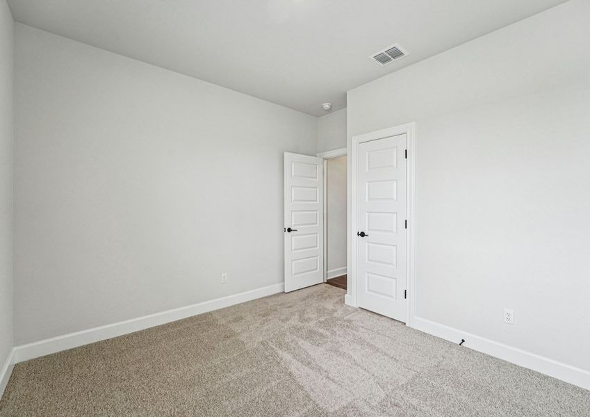 Spacious carpeted bedroom featuring a window with natural light and a doorway to the ensuite master bath. Spacious carpeted bedroom featuring a window with natural light and a doorway to the ensuite master bath.
