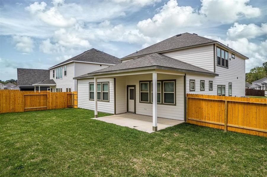 A different view of the covered patio highlights its generous size and potential for various outdoor furnishings. The surrounding green space and fence add to the charm and functionality of this inviting backyard area, perfect for enjoying the outdoors in comfort. Photos are from another Rylan floor plan.