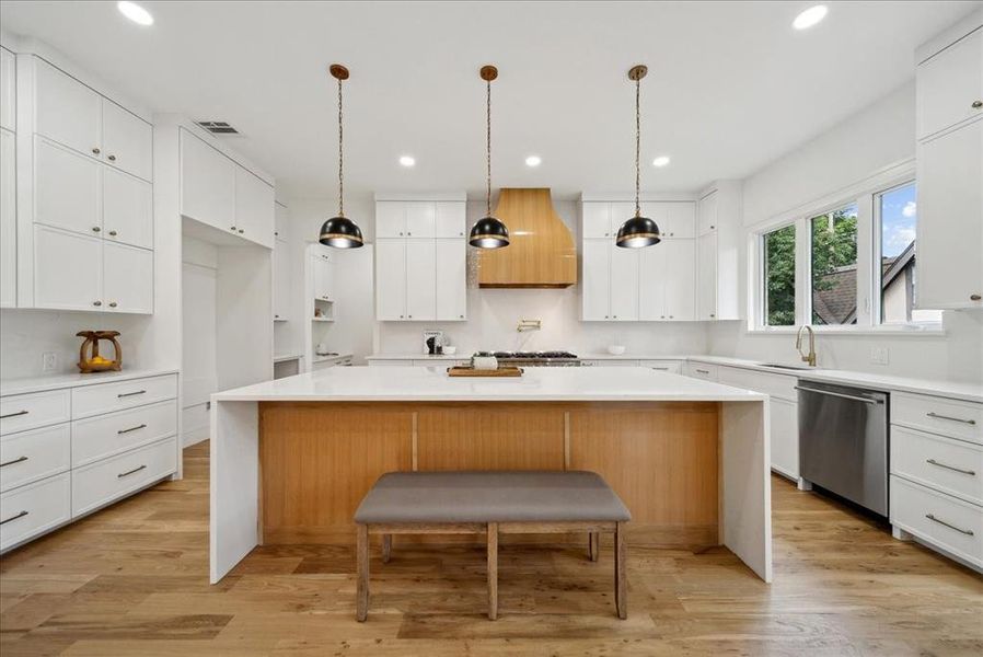 Kitchen with white cabinets, light hardwood floors, a kitchen island, and stainless steel dishwasher